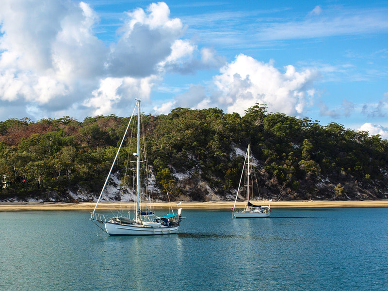 Picture shows Platypus Bay near Hervey Bay and Pinnacle estate. Image has two sailing boats, calm water and Fraser Island. 